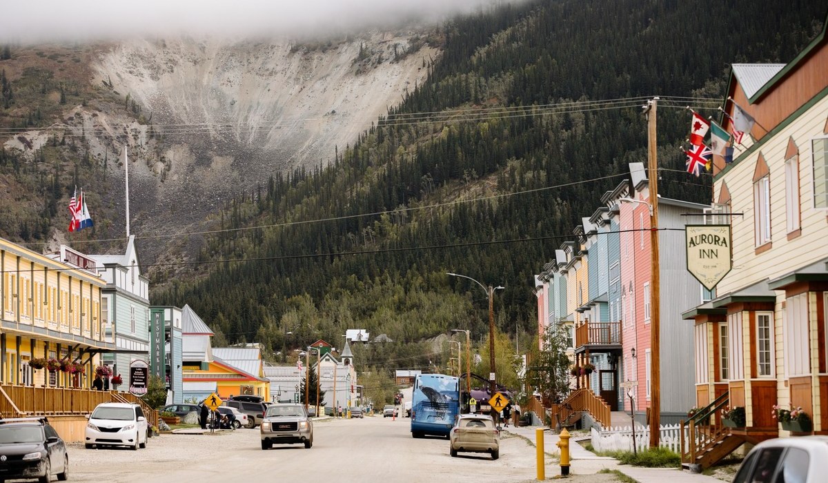Downtown Dawson City, Yukon, with colourful historic buildings, a tour coach and a forested mountain rising behind the street.